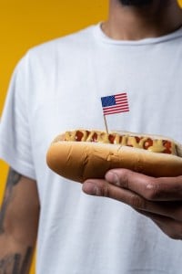 A scrumptious bratwurst, generously slathered with vibrant, golden mustard, proudly adorned with a tiny american flag impaled by a toothpick, a visual symphony of flavors and patriotism.