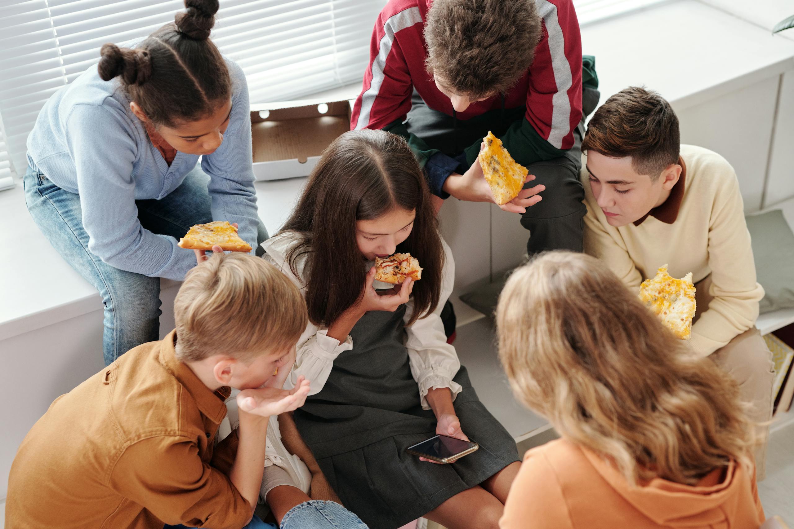 A children eating pizza while looking the smartphone