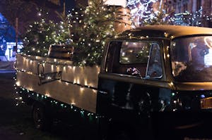 A vintage truck adorned with Christmas lights and trees, creating a festive atmosphere at night.