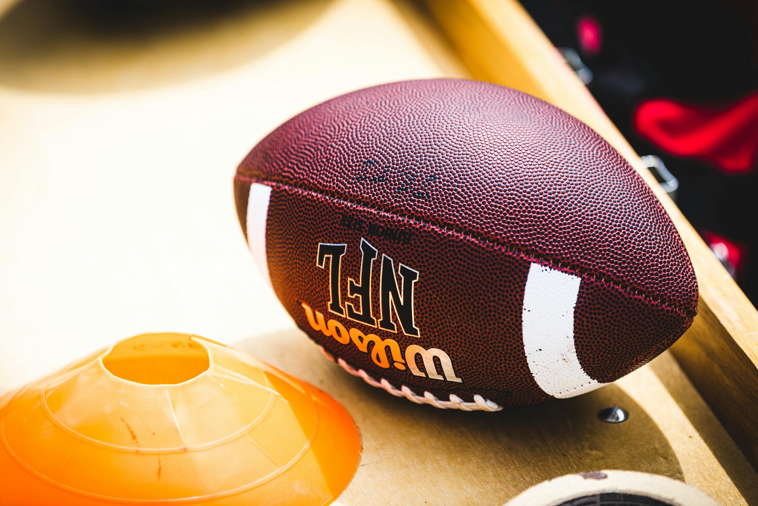 An American football placed on a training bench next to an orange training cone, ideal for sports concept.