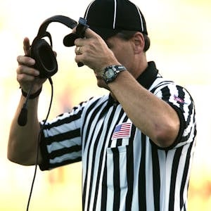 Football referee in uniform adjusting headset during a game outdoors.